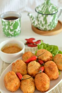 Close-up of fried croquettes with chili peppers, tea, and sauce on a table.