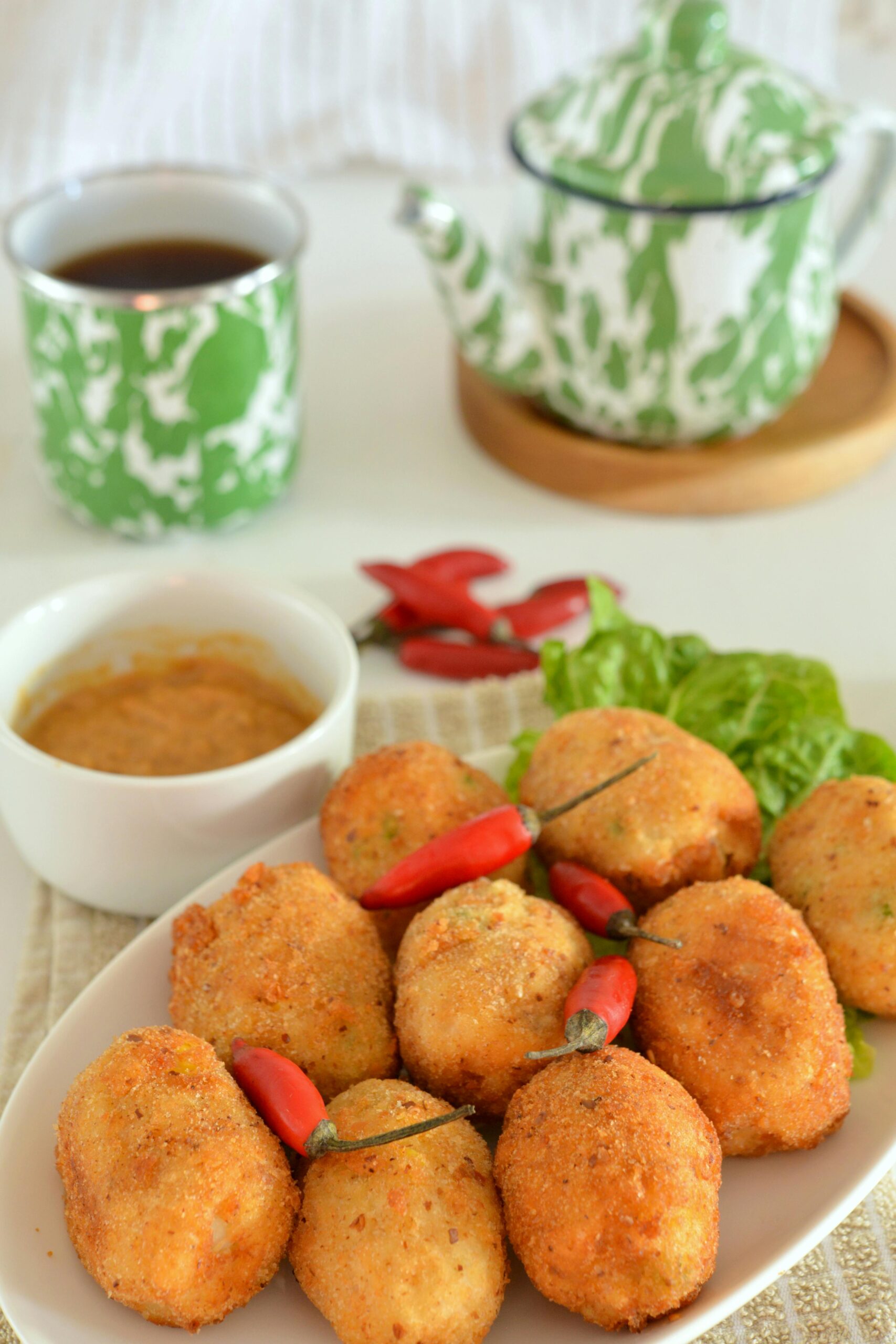 Close-up of fried croquettes with chili peppers, tea, and sauce on a table.